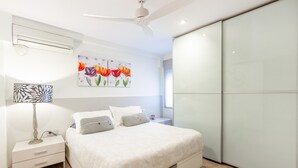 A modern bedroom with a bed, bedside tables, a ceiling fan, and a large window.
