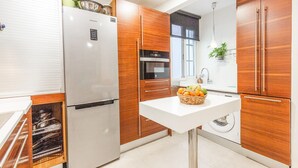 A modern kitchen with a stainless steel refrigerator, wooden cabinets, a built-in oven, a sink, and a washing machine.