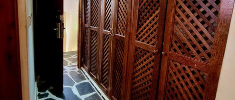 Um corredor com piso de pedra estampada, portas de madeira com desenhos em treliça e um ventilador de teto.
