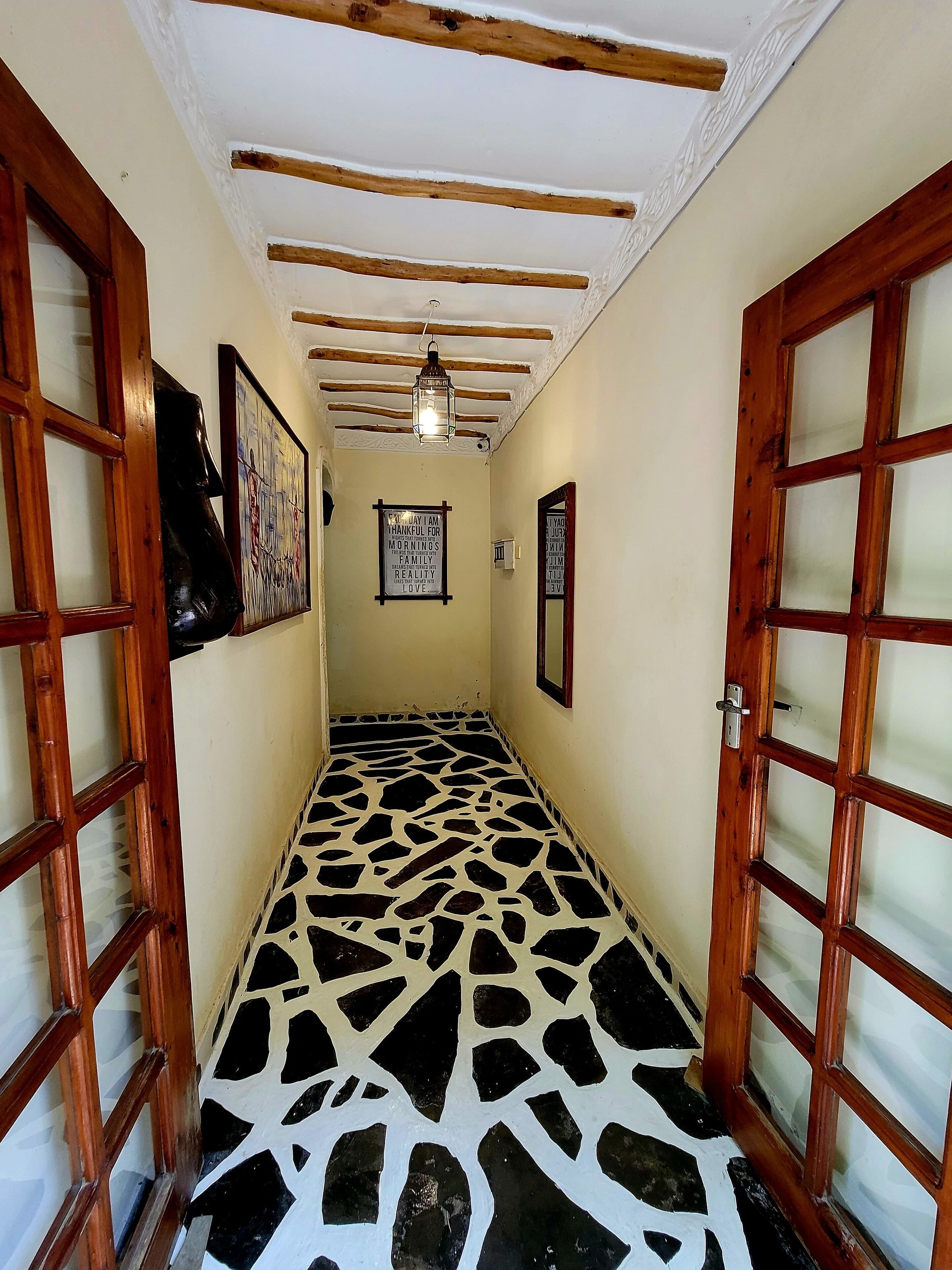Um corredor com chão estampado, portas de madeira e teto com vigas aparentes.