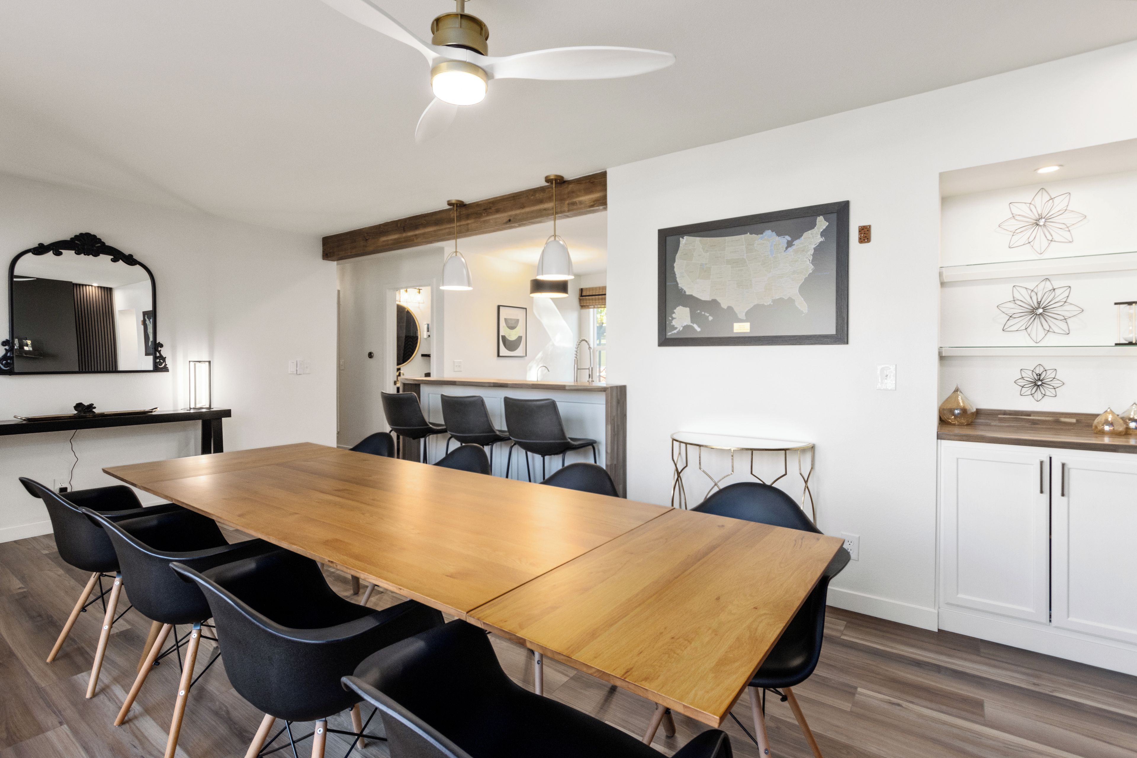 Een moderne eethoek met een houten tafel, zwarte stoelen, hanglampen en een plafondventilator.