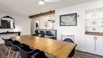 Een moderne eethoek met een houten tafel, zwarte stoelen, hanglampen en een plafondventilator.