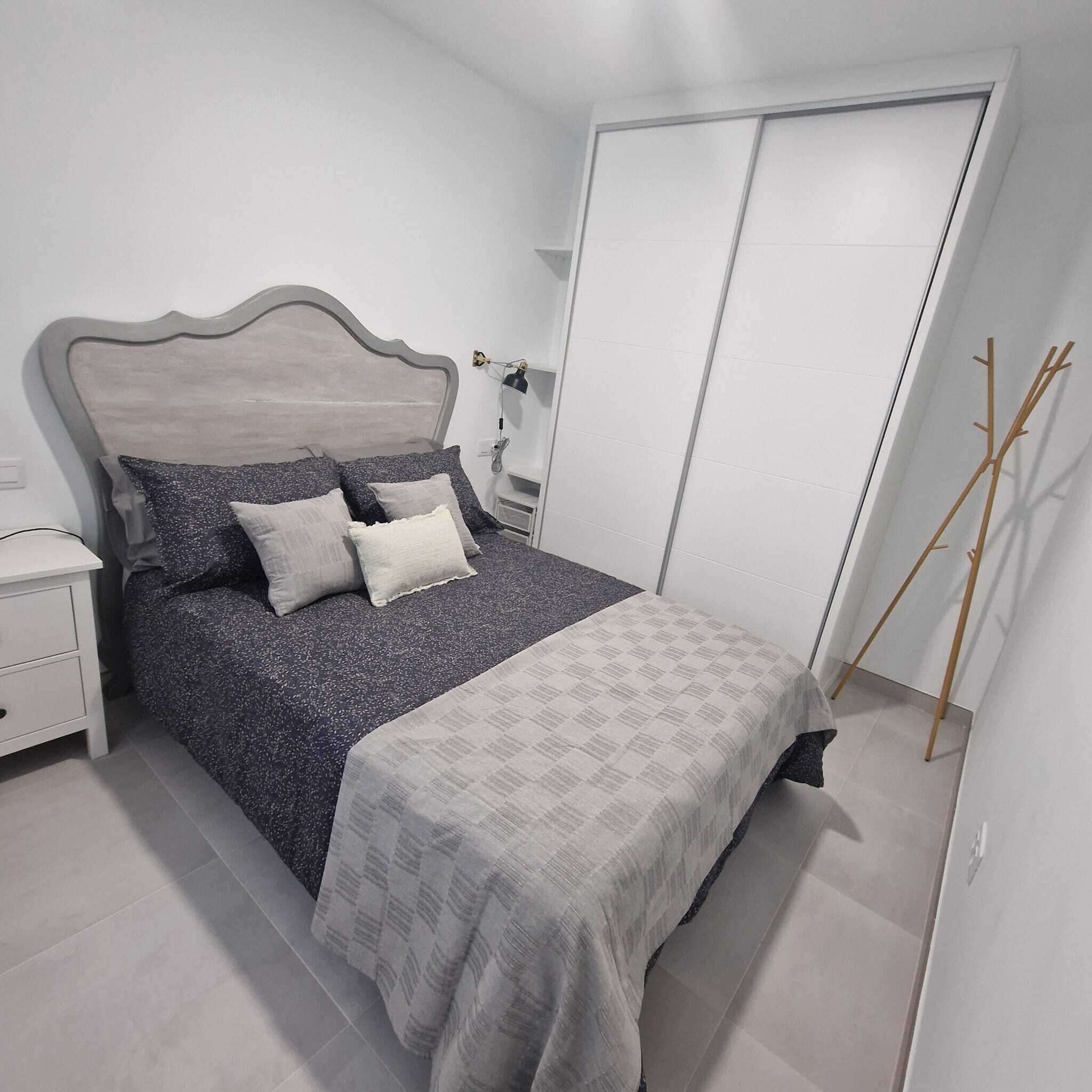 A bedroom with a bed, nightstand, bedside table, lamp, and a wardrobe.