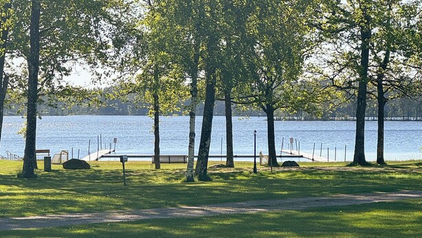A lakeside park with a bench, a lamp post, and a path leading to a dock.