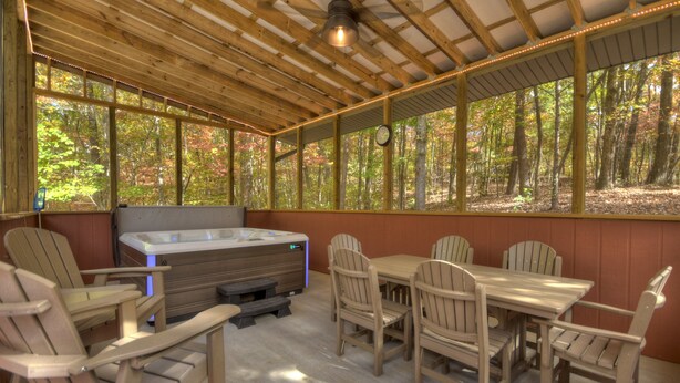 Un espacio de estar al aire libre cubierto con sillas y una mesa de madera, un jacuzzi y vistas a un bosque.