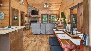 A cozy cabin interior with a stone fireplace, wooden walls, a dining area with benches, and a television mounted above the fireplace. - Squirrels Hideaway | Fire Pit | MTN Views (Copperhill)