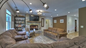 A spacious living room with a stone fireplace, leather sofas, a television, and a bookshelf.