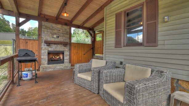 A covered deck with wicker furniture, a stone fireplace, and a grill.