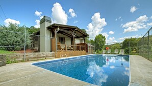 A swimming pool with a wooden deck and lounge chairs, surrounded by a fence and trees.