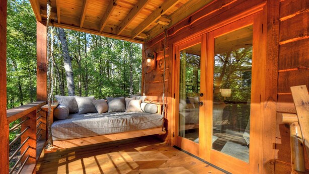 Uma cabana de madeira com cama embutida, janelas amplas e um deck.