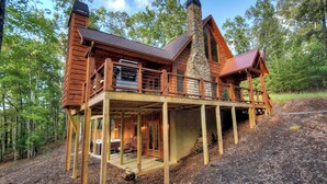 Uma cabana de madeira com chaminé de pedra, um deck e varanda com mobiliário ao ar livre.
