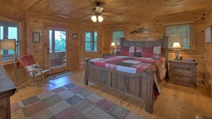 A wooden cabin bedroom with a bed, rocking chair, and a ceiling fan. - Vistas Over Aska | Pet Friendly | MTN Views | Outdoor Fireplace | (Blue Ridge)