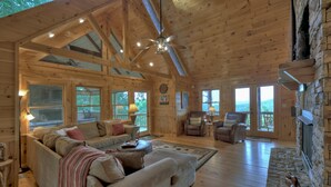 A spacious wooden cabin with a large living area, a stone fireplace, and large windows offering views of the outdoors. - Vistas Over Aska | Pet Friendly | MTN Views | Outdoor Fireplace | (Blue Ridge)