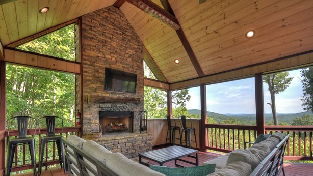 A covered deck with a stone fireplace, outdoor seating, and a view of the mountains. - Vistas Over Aska | Pet Friendly | MTN Views | Outdoor Fireplace | (Blue Ridge)
