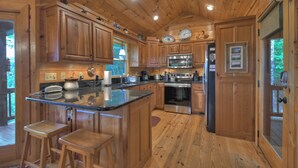 A wooden cabin kitchen with a central island, bar stools, stainless steel appliances, and wooden cabinets. - Vistas Over Aska | Pet Friendly | MTN Views | Outdoor Fireplace | (Blue Ridge)