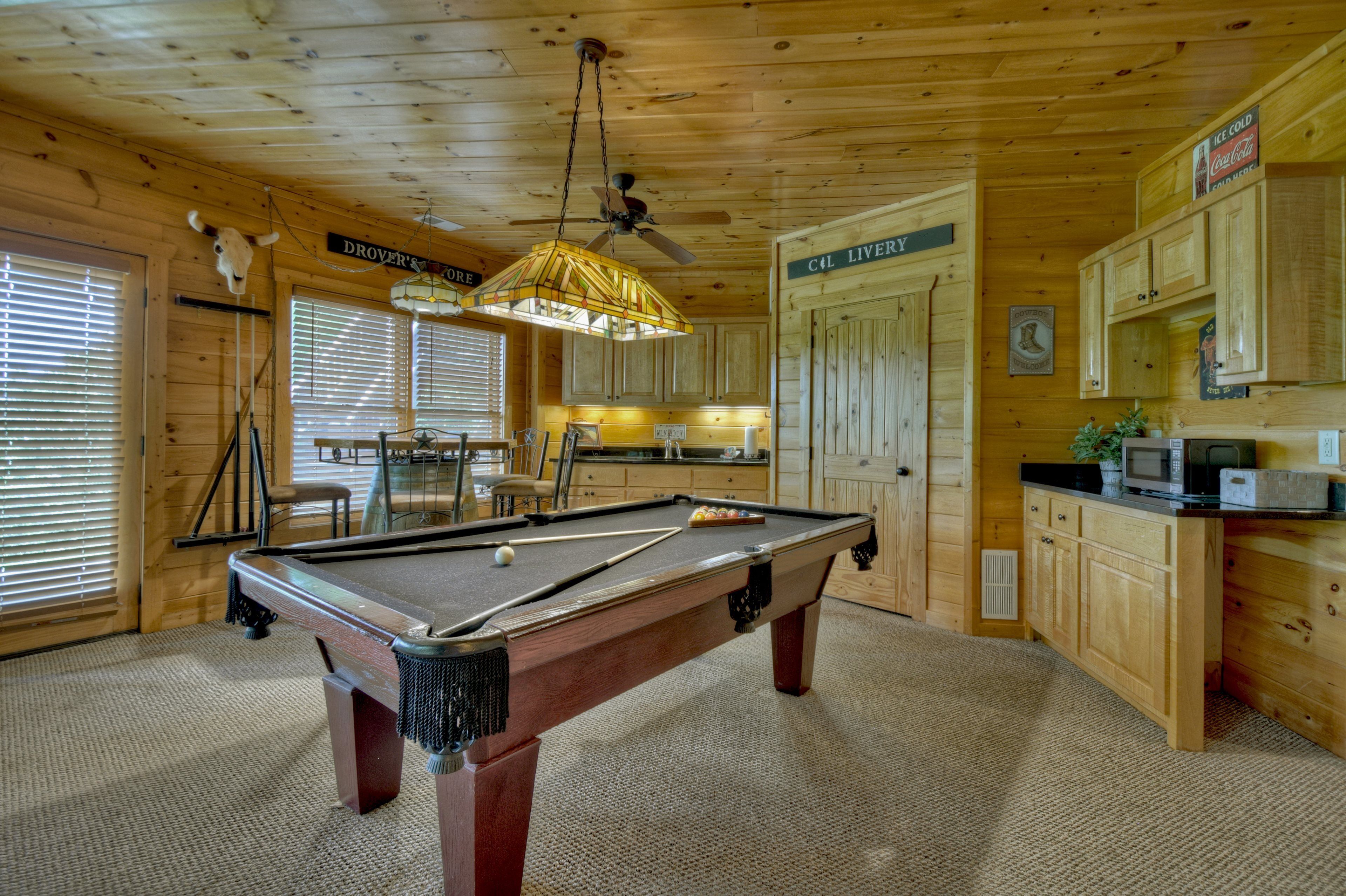 A pool table in a wooden room with a ceiling fan, a billiards rack, and a billiard cue.