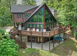 A log cabin with a balcony, outdoor seating, and a stone fireplace.