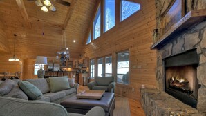 A cozy cabin interior with a stone fireplace, wooden walls, and large windows. - Stokes Haven | Pet Friendly | Hot Tub | Creek (McCaysville)