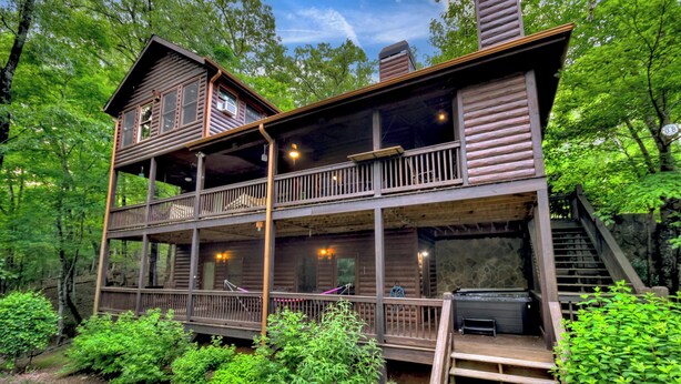 A two-story log cabin with a balcony and a fireplace on the ground floor. - Stokes Haven | Pet Friendly | Hot Tub | Creek (McCaysville)