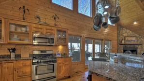 A spacious kitchen with wooden cabinets, stainless steel appliances, granite countertops, and large windows. - Stokes Haven | Pet Friendly | Hot Tub | Creek (McCaysville)