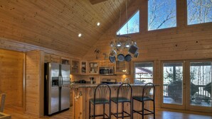 A wooden cabin kitchen with a central island, stainless steel appliances, and large windows. - Stokes Haven | Pet Friendly | Hot Tub | Creek (McCaysville)