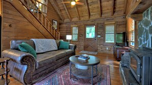 Ein Blockhaushaus-Interieur mit Ledersofa, rundem Couchtisch, Kamin und einer Treppe.