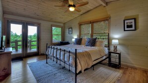Ein Schlafzimmer mit Bett, Nachttisch, Deckenventilator und Blick ins Freie durch eine Tür.