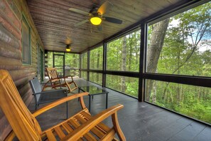 A cabin with large windows, wooden furniture, and a ceiling fan.