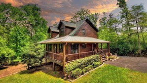 A two-story log cabin with a porch, surrounded by dense forest.