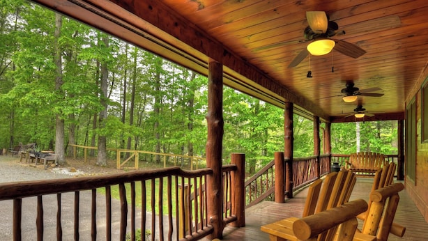 A wooden deck with chairs and a railing overlooking a forest.
