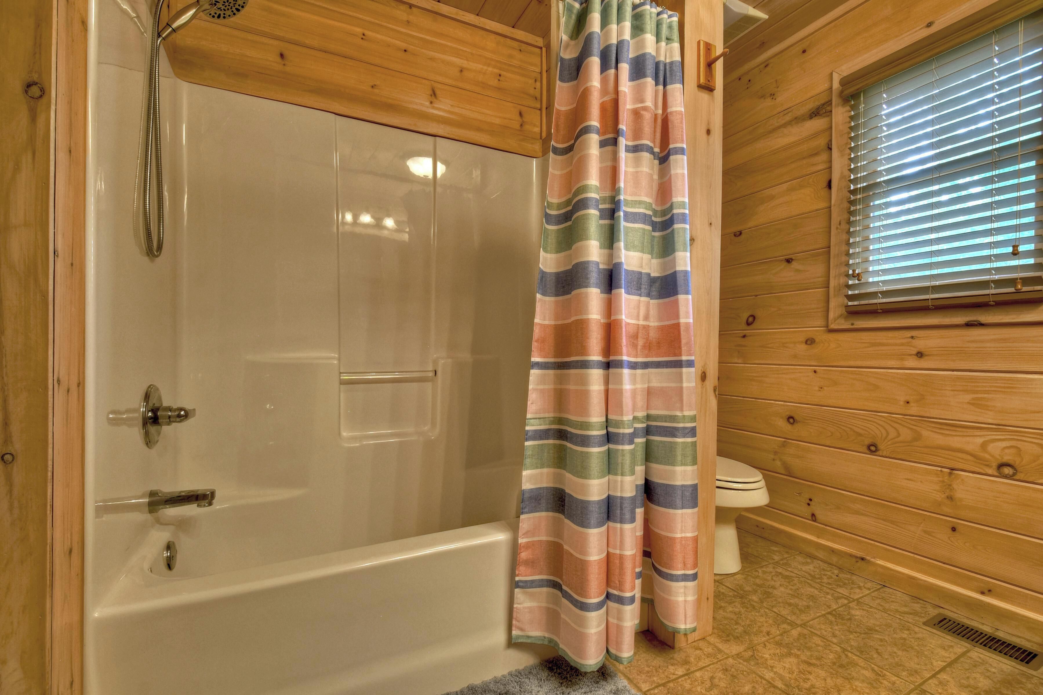 A wooden cabin bathroom with a shower, toilet, and a window with blinds.