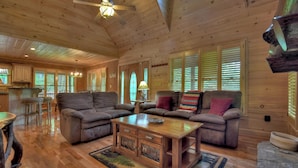 A spacious wooden cabin with a large living area featuring two sofas, a coffee table, and a dining table.