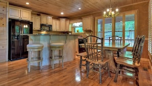 A rustic kitchen with wooden cabinets, a central island with stools, a chandelier, and a dining table with chairs.