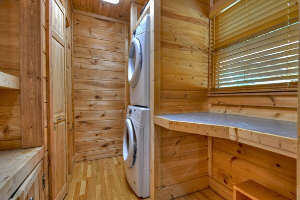 Interior de una cabaña de madera con lavadora, armarios de madera y una ventana con persianas.