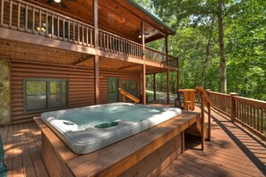 Una cabaña de madera con un jacuzzi en la terraza, rodeada de árboles.