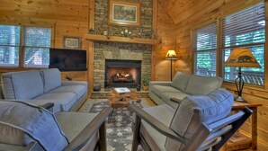 Ein gemütliches Blockhaus-Interieur mit Kamin aus Stein, zwei Sofas, einem Fernseher und einer Lampe.