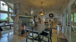 A cozy cabin interior with a stone fireplace, wooden dining table, and a view of the outdoors. - Champagne Chalet | MTN Views | Hot Tub | Secluded (Morganton)