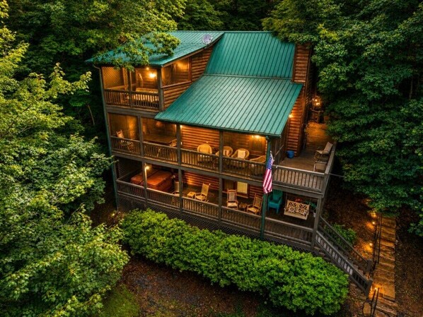 A multi-story log cabin with a green roof, surrounded by dense forest.