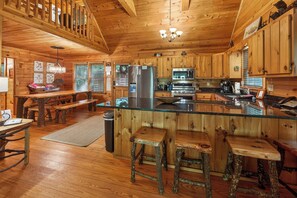 A wooden cabin interior with a kitchen, dining area, and bar seating.