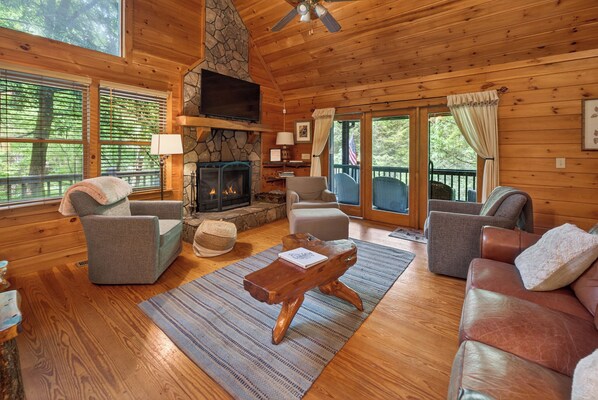 A cozy cabin interior with a stone fireplace, wooden walls, and a comfortable seating area.