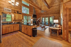 A cabin with wooden interiors, a kitchen with a stone fireplace, a dining area with a table and chairs, and large windows.