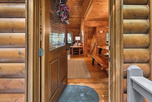 A wooden cabin interior with a wooden door, a bench, a table, and a fireplace.