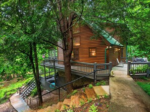 A log cabin with a wooden deck, a staircase, and a small porch area.