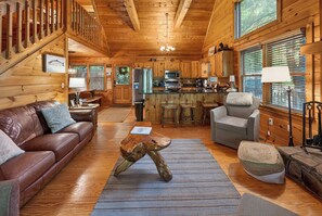 A wooden cabin interior with a living room, kitchen, and dining area.