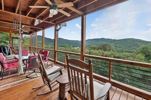 A wooden deck with a table and chairs, a ceiling fan, and a view of green hills. - Shepherd's Sky View | Secluded | MTN Views | Pool Table | (Morganton)