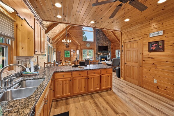 A spacious kitchen with wooden cabinets, granite countertops, and a stone fireplace. - Shepherd's Sky View | Secluded | MTN Views | Pool Table | (Morganton)
