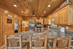 A wooden cabin interior with a kitchen featuring granite countertops, wooden cabinets, and a central island with bar stools.
