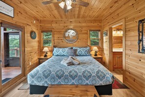 A wooden cabin bedroom with a bed, two nightstands, a ceiling fan, and a large window.