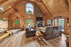 L’intérieur d’une cabane en rondins, avec une cheminée, des meubles en bois et de grandes fenêtres.