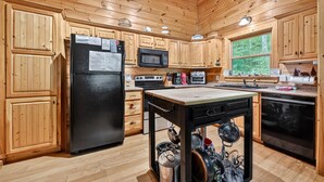 A wooden cabin kitchen with a refrigerator, microwave, stove, and wooden cabinets.